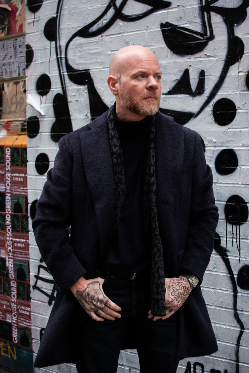 Carl Reader, dark coat, graffiti wall